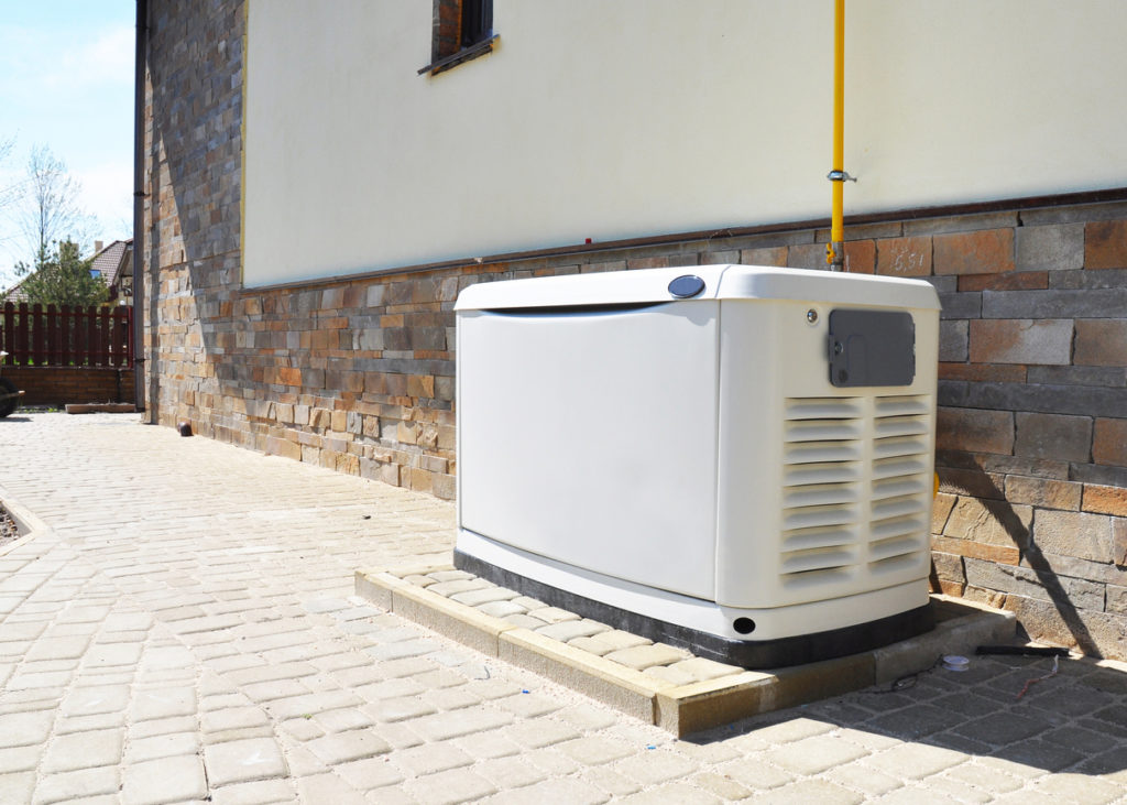 Generator located on the side of a brick and siding building. The generator is white.